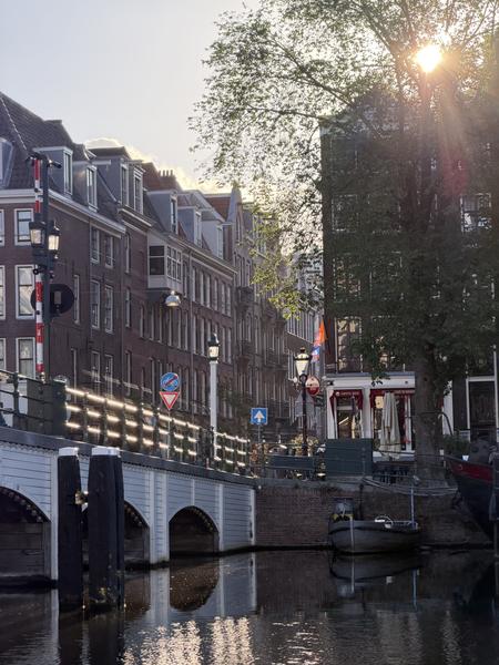 This photo captures a serene golden hour scene along the Amstel canal in Centrum, Amsterdam, showcasing historic canal houses and a charming bridge reflecting in the calm water